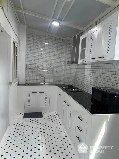 Modern white kitchen with sleek cabinets and black countertop, featuring a gas stove and microwave.