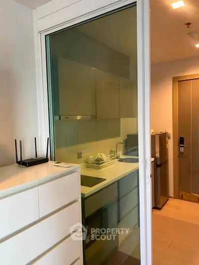 Modern compact kitchen with sleek cabinetry and glass sliding door in a stylish apartment.