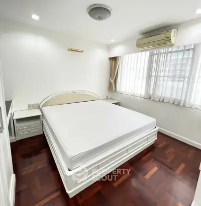 Spacious bedroom with large window and wooden flooring in modern apartment