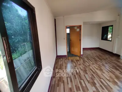 Spacious room with wooden flooring and large windows offering natural light.