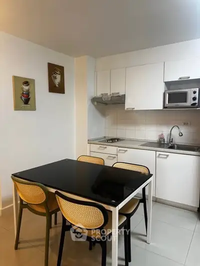Modern kitchen with sleek white cabinets and dining area, featuring a black glass table and stylish chairs.