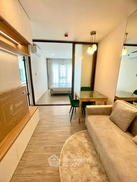 Modern living room with cozy sofa, dining area, and view into bedroom through glass partition.