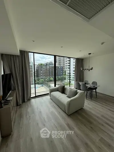 Modern living room with large windows and city view, featuring elegant decor and dining area.