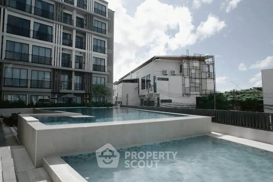 Modern apartment building with luxurious outdoor pool and clear blue sky.