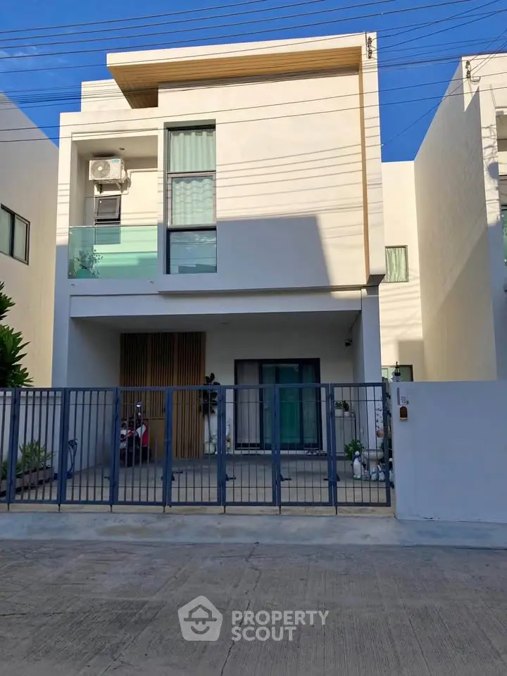 Modern two-story house with sleek design and gated entrance, featuring a balcony and air conditioning unit.