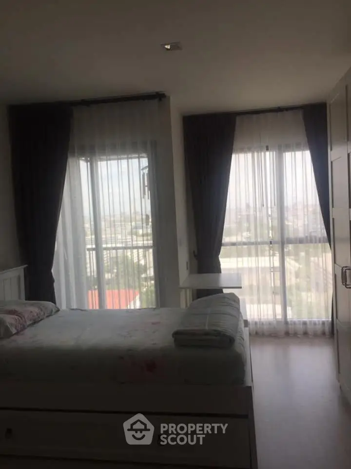 Bright bedroom with large windows and sheer curtains offering a scenic view, featuring a cozy bed and modern decor.