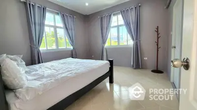 Spacious bedroom with large windows and natural light, featuring modern curtains and tiled flooring.