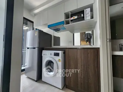 Modern kitchen with washing machine, fridge, and microwave in sleek apartment.