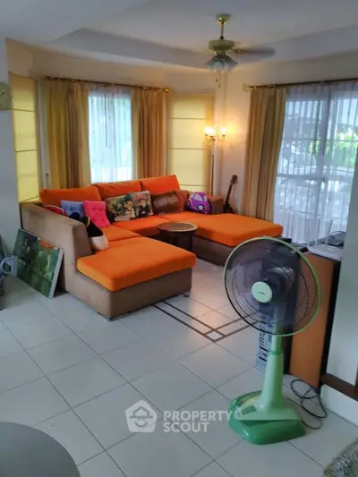 Spacious living room with vibrant orange sectional sofa and large windows for natural light.