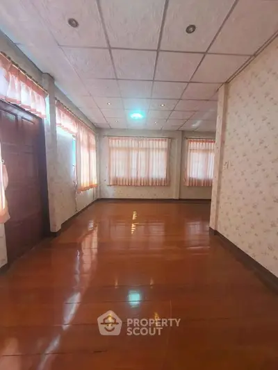 Spacious room with wooden flooring and large windows in a cozy home.