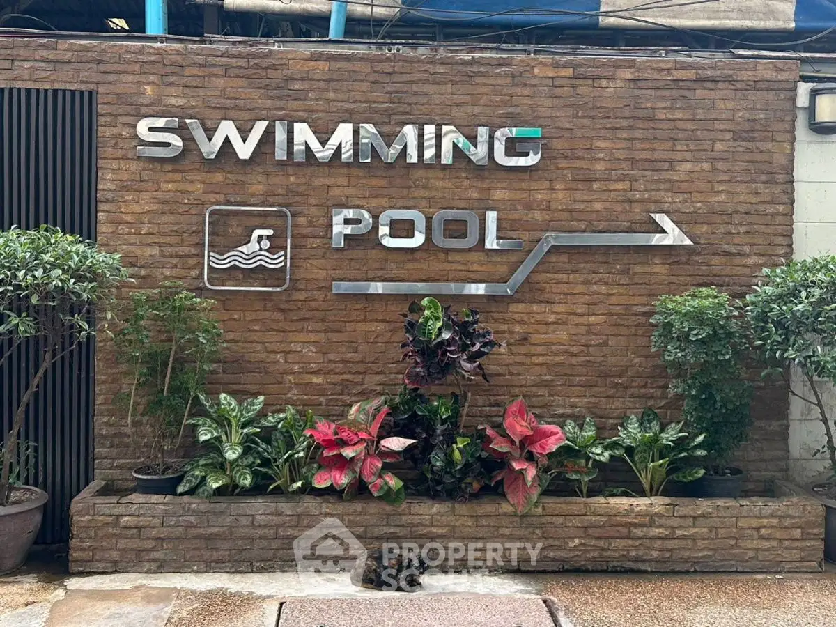 Charming swimming pool entrance with lush greenery and stylish signage.