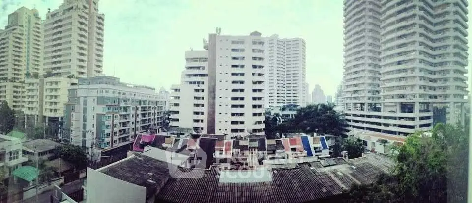 Panoramic view of urban high-rise buildings with lush greenery and rooftops.