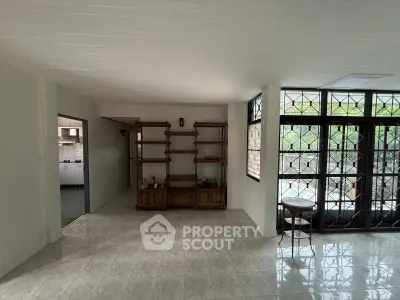 Spacious living area with large windows and tiled flooring, leading to a kitchen with modern appliances.