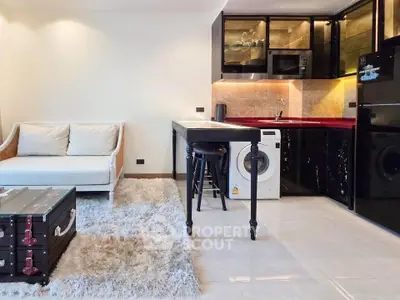 Modern open-layout living room with kitchen, featuring sleek black cabinets, washing machine, and cozy seating area.