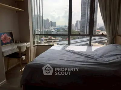 Modern bedroom with city view, large windows, and cozy workspace in urban apartment.