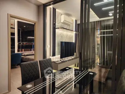 Modern living room with sleek decor and glass dining table, featuring a view into a stylish bedroom.