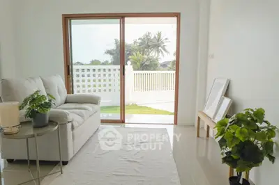 Bright living room with sliding doors leading to a lush garden view, featuring cozy sofa and indoor plants.