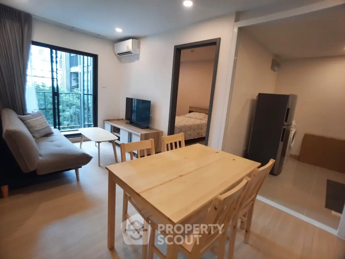 Modern apartment interior with open living and dining area, featuring a cozy sofa and large window view.