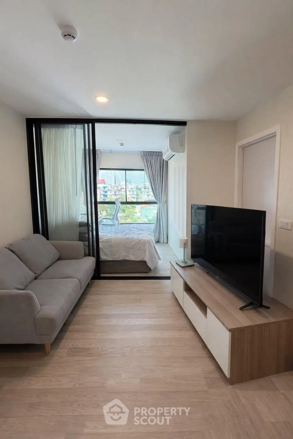 Modern living room with sleek furniture and view into a cozy bedroom, featuring a large TV and stylish decor.
