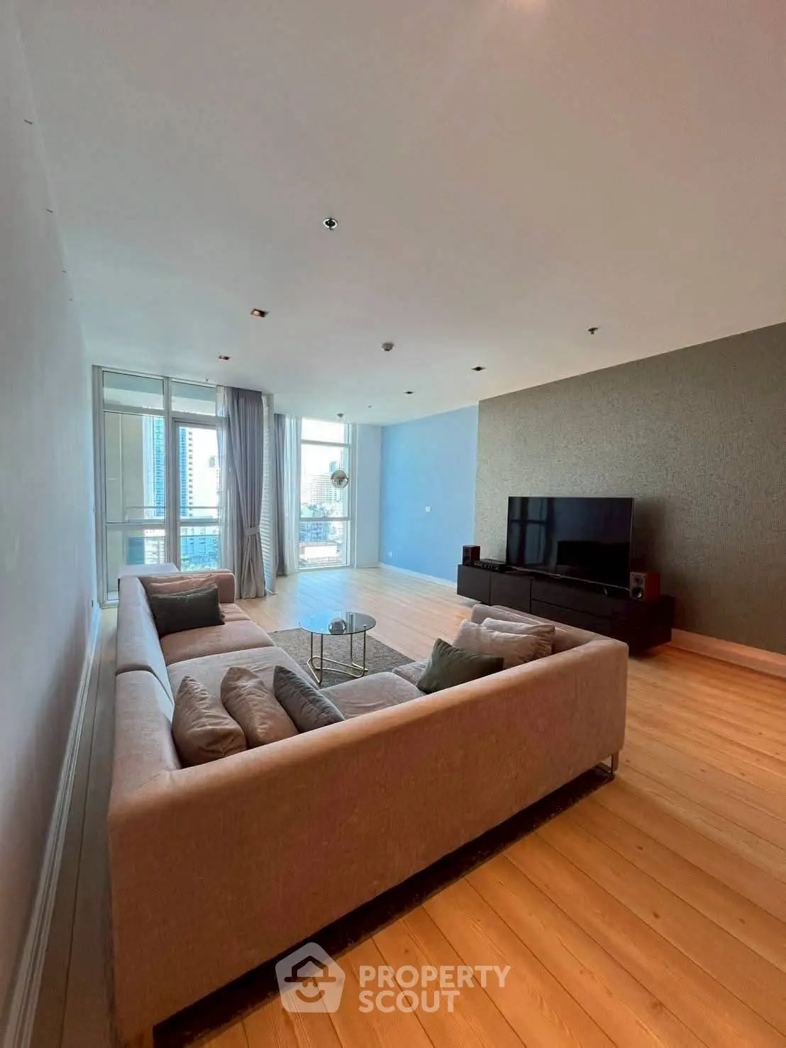 Spacious modern living room with large sofa and TV, featuring city view.