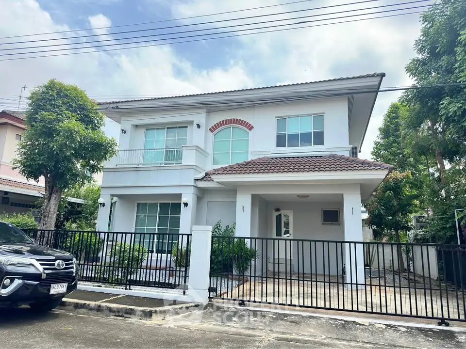 Charming two-story house with gated driveway and lush greenery in a serene neighborhood.