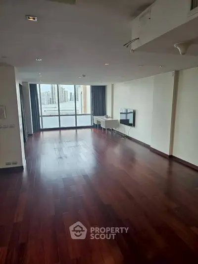Spacious living room with hardwood floors and large windows offering city views.