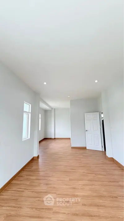 Spacious empty room with wooden flooring and white walls, perfect for customization.