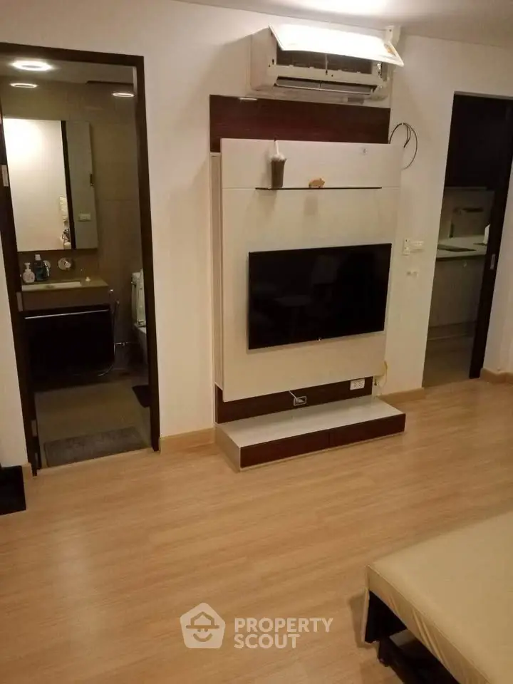 Modern living room with wall-mounted TV and air conditioning, adjacent to a sleek bathroom and kitchen.