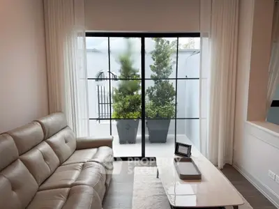 Modern living room with leather sofa and large window overlooking a serene balcony garden.