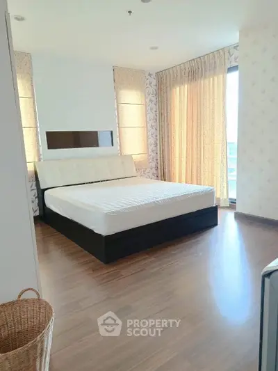 Spacious bedroom with large windows and elegant decor, featuring a comfortable bed and wooden flooring.
