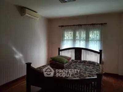 Cozy bedroom with wooden bed frame and air conditioning, featuring natural light through sheer curtains.