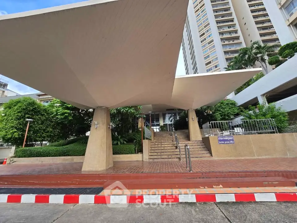 Modern building entrance with unique architectural design and lush greenery.