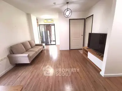 Spacious living room with modern decor and large TV, featuring wooden flooring and ample natural light.