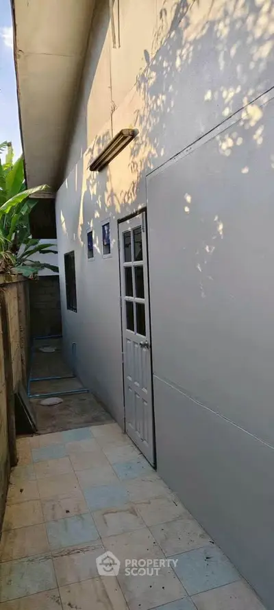 Narrow exterior side passage with tiled flooring and white door