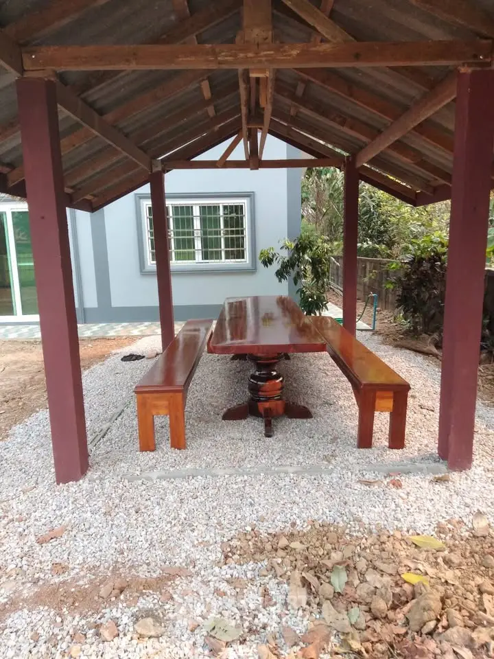 Charming outdoor gazebo with wooden table and benches, perfect for relaxation in a serene garden setting.