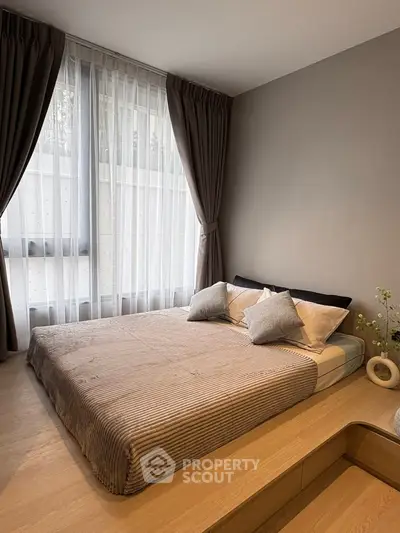 Cozy bedroom with large window and elegant curtains, featuring a comfortable bed and stylish decor.