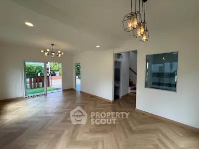 Spacious modern living room with stylish lighting and wooden flooring, opening to a lush garden view.