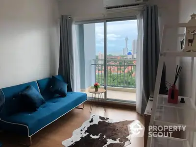 Modern living room with balcony and city view, featuring stylish blue sofa and cowhide rug.