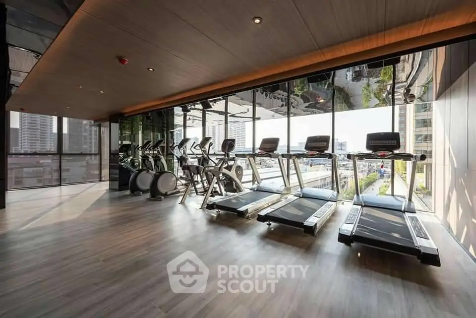 Modern gym with city view featuring treadmills and exercise bikes in a high-rise building.