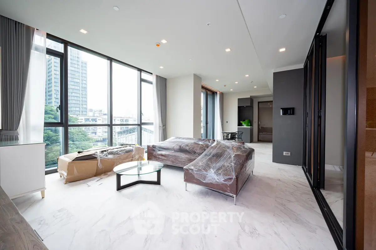 Spacious modern living room with large windows and city view, featuring sleek furniture and elegant decor.