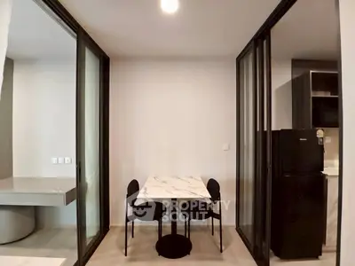 Modern dining area with sleek table and chairs, adjacent to a compact kitchen with refrigerator.