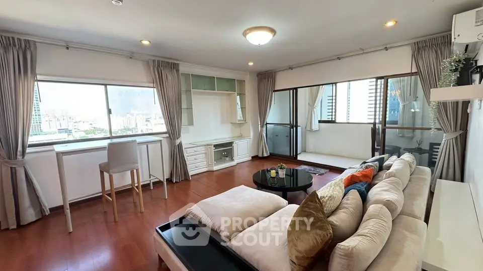 Spacious living room with large windows and balcony offering stunning city views.