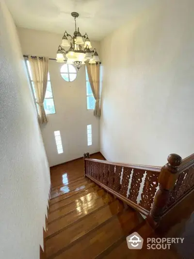 Elegant wooden staircase with ornate railing and chandelier in bright home interior.