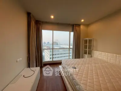 Spacious bedroom with city view and modern furnishings in high-rise apartment.