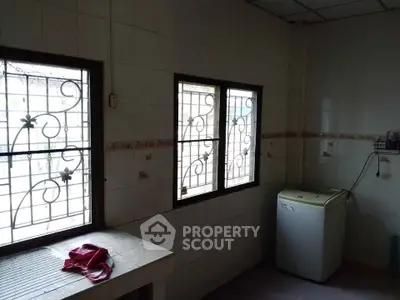 Cozy kitchen space with washing machine and natural light from barred windows.