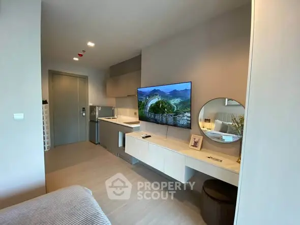 Modern studio apartment with sleek design, featuring a wall-mounted TV, compact kitchen, and stylish decor.