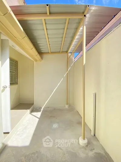 Bright outdoor patio with covered roof and beige walls, perfect for relaxation.