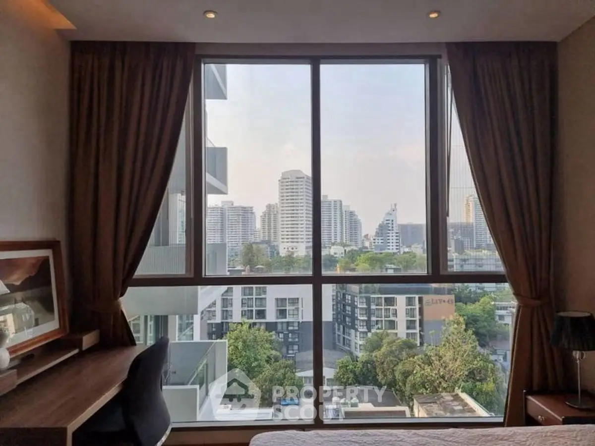 Stunning city view from a modern bedroom window with elegant curtains and a cozy desk setup.