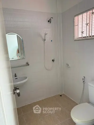 Minimalist bathroom with shower, sink, and toilet in a tiled setting.