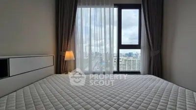 Modern bedroom with city view, featuring a large window and elegant curtains.